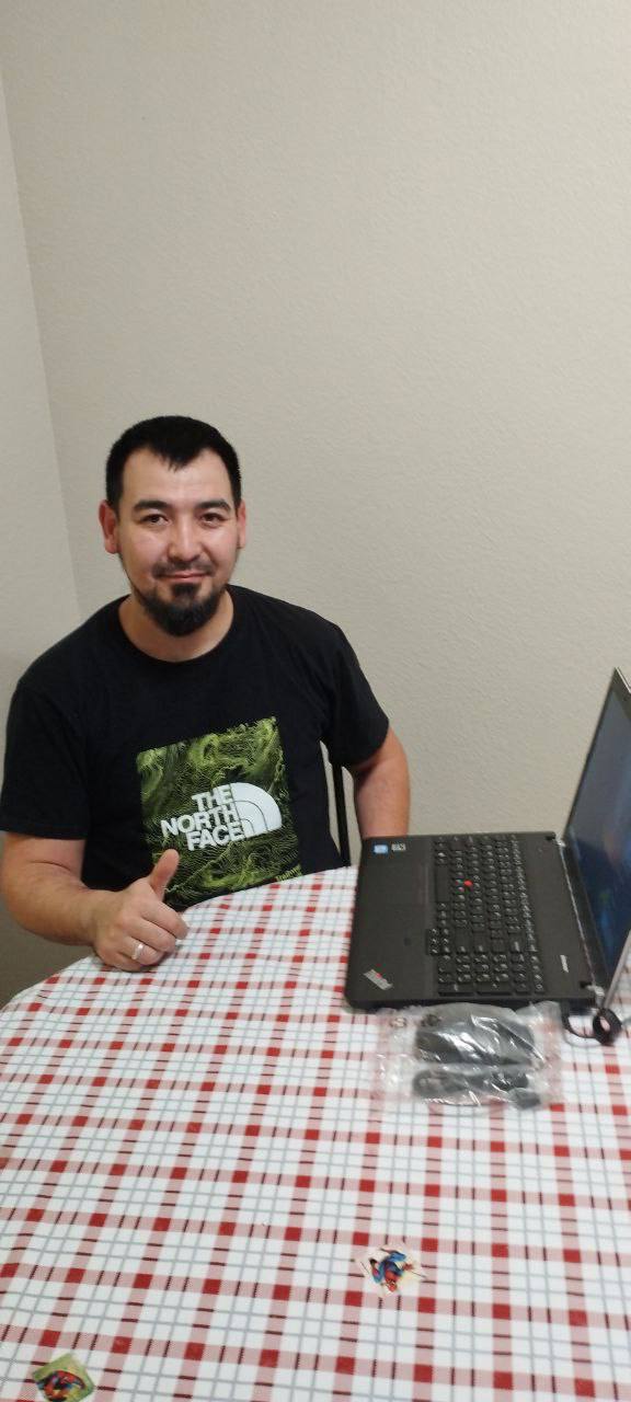 A man smiles while looking at a laptop on a patterned tablecloth.
