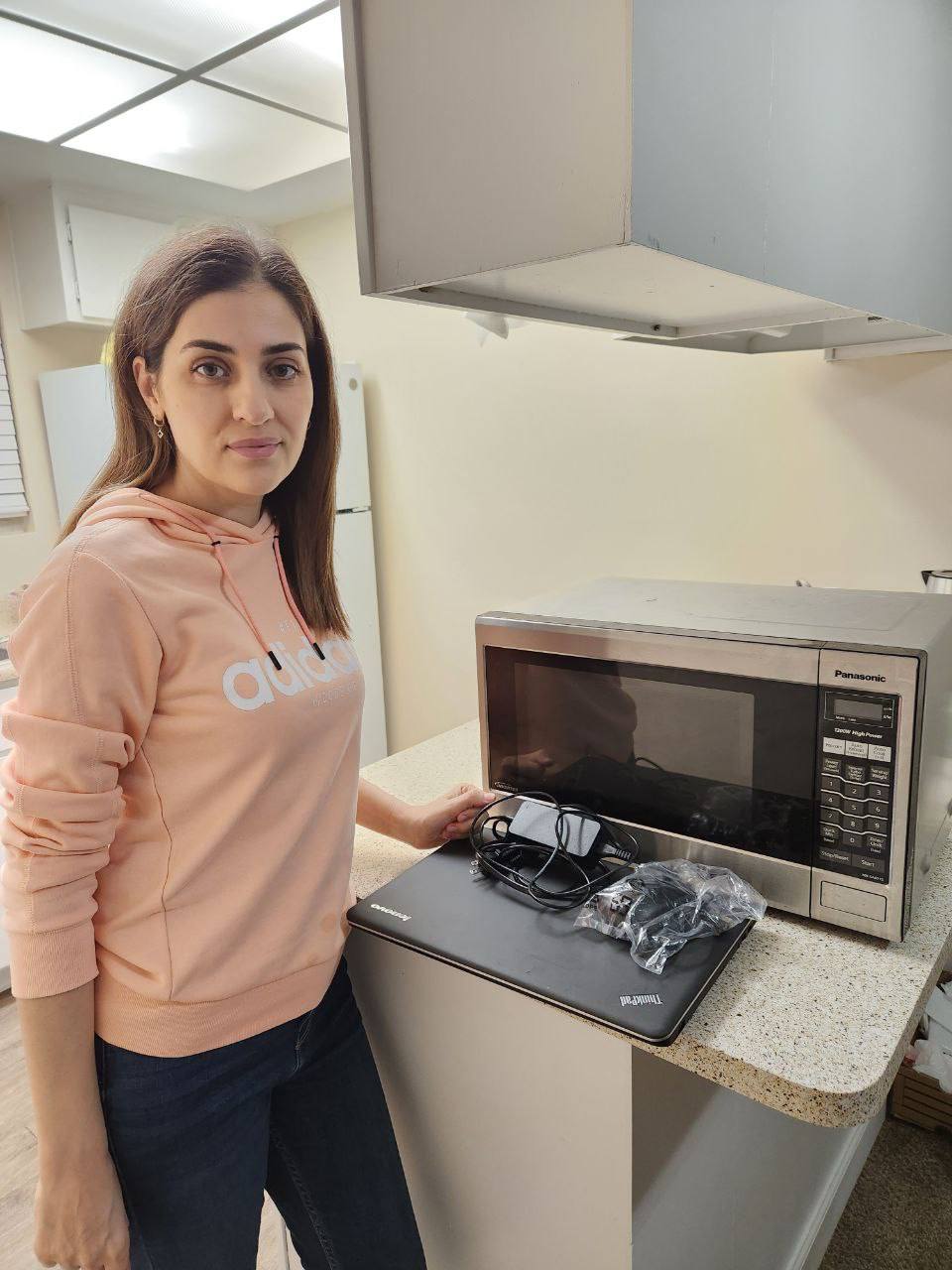 A smiling woman holds a phone while standing in a bright, modern kitchen.